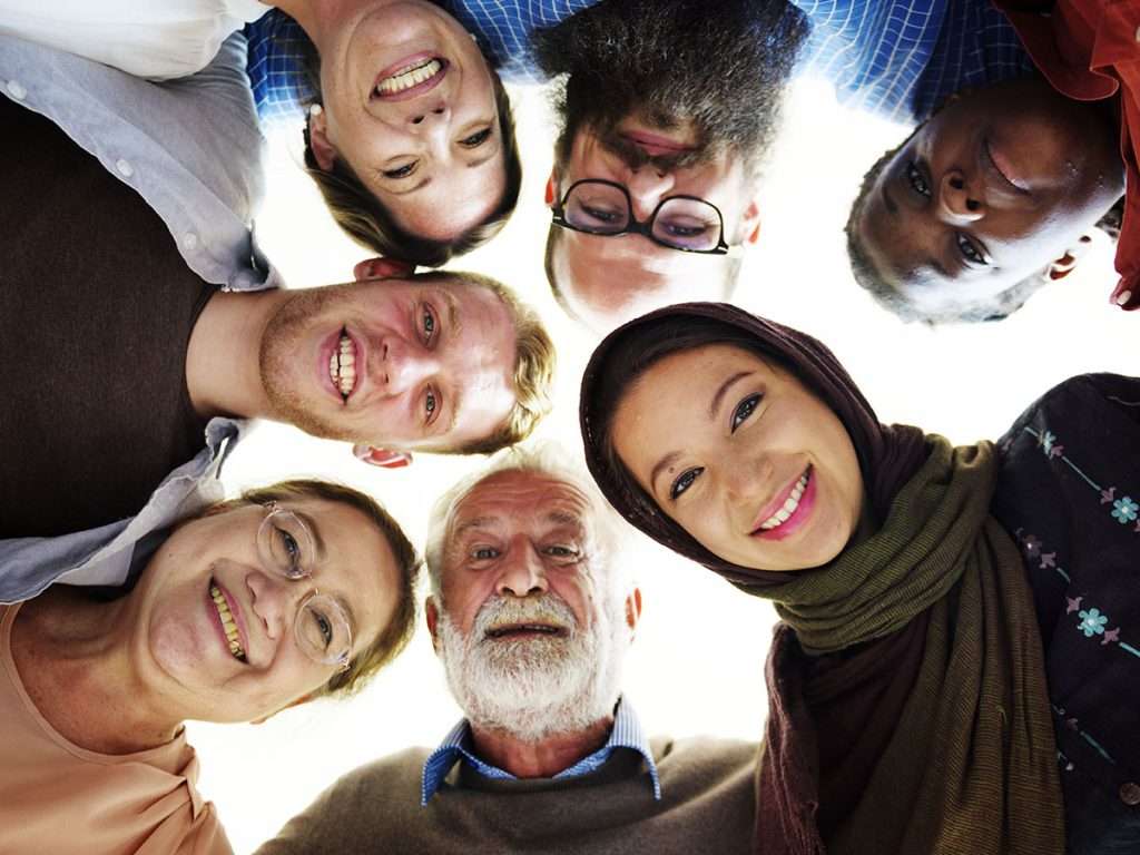 A diverse group of people of different ages and backgrounds standing in a circle, smiling down at the camera.