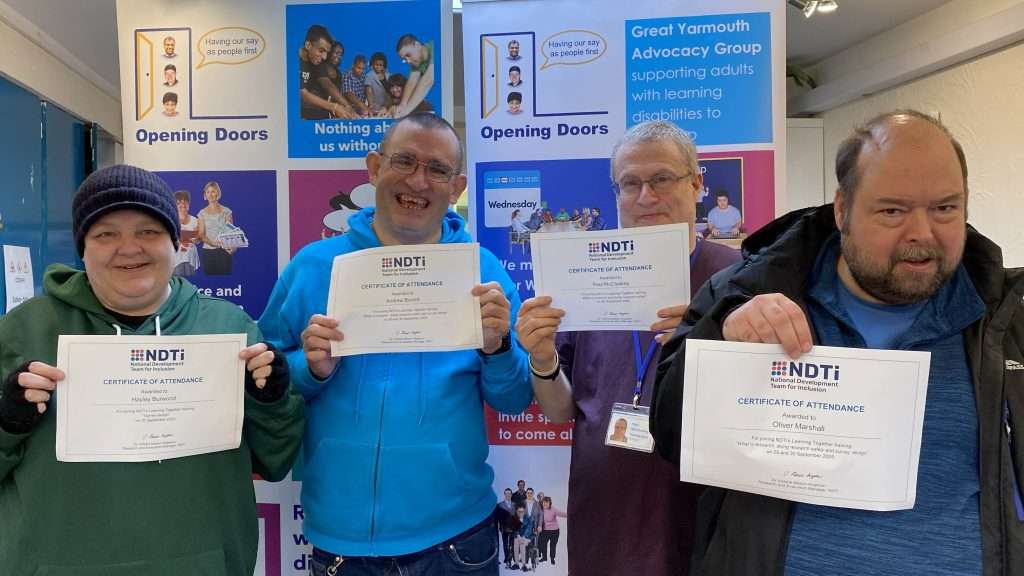 Four of the learners at Opening Doors Norwich with certificates in hand and smiling at the camera.