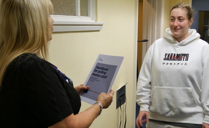 Two people outside a polling station. One is gathering information.