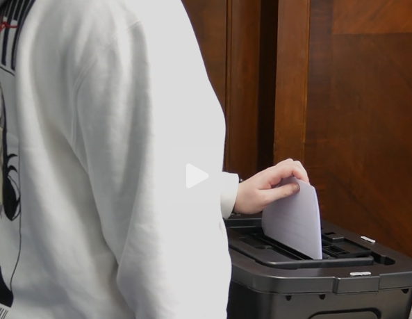 A person is placing a ballot paper into a black ballot box.