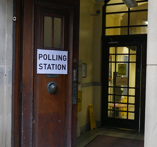 A doorway into a community building. There is a temporary sign on the door that says Polling Station.
