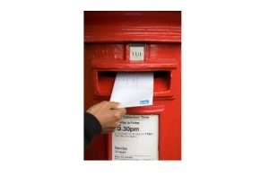 Someone putting a letter into a red post box.